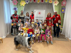 Children and adults pose for a photo in front of a red cross banner holding donations from IDDT
